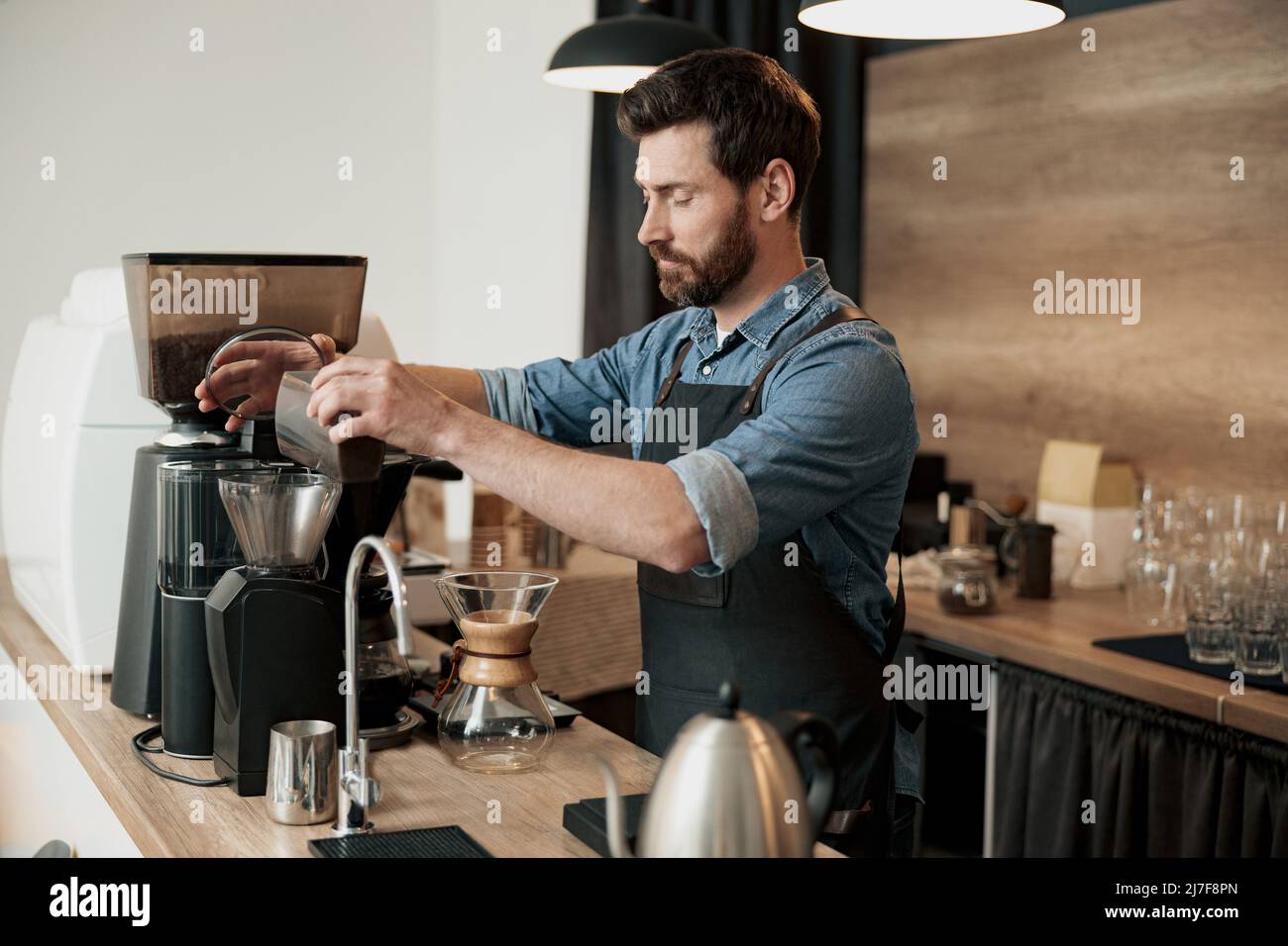 Le beau barista moud les grains de café dans la cafetière Banque D'Images