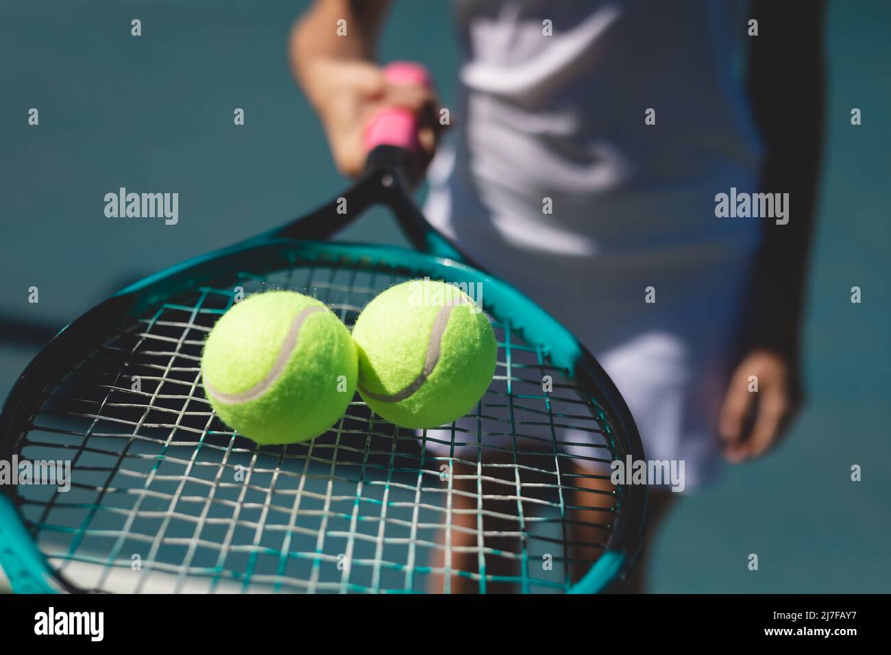 Balles de tennis sur une raquette tenue par une jeune femme caucasienne debout sur le terrain par temps ensoleillé Banque D'Images