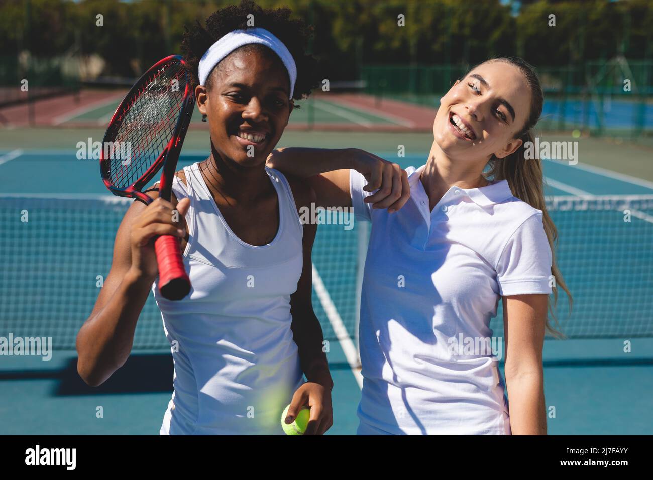 Portrait d'athlètes biraciaux heureux debout sur le court de tennis tout en prenant une pause le jour ensoleillé Banque D'Images