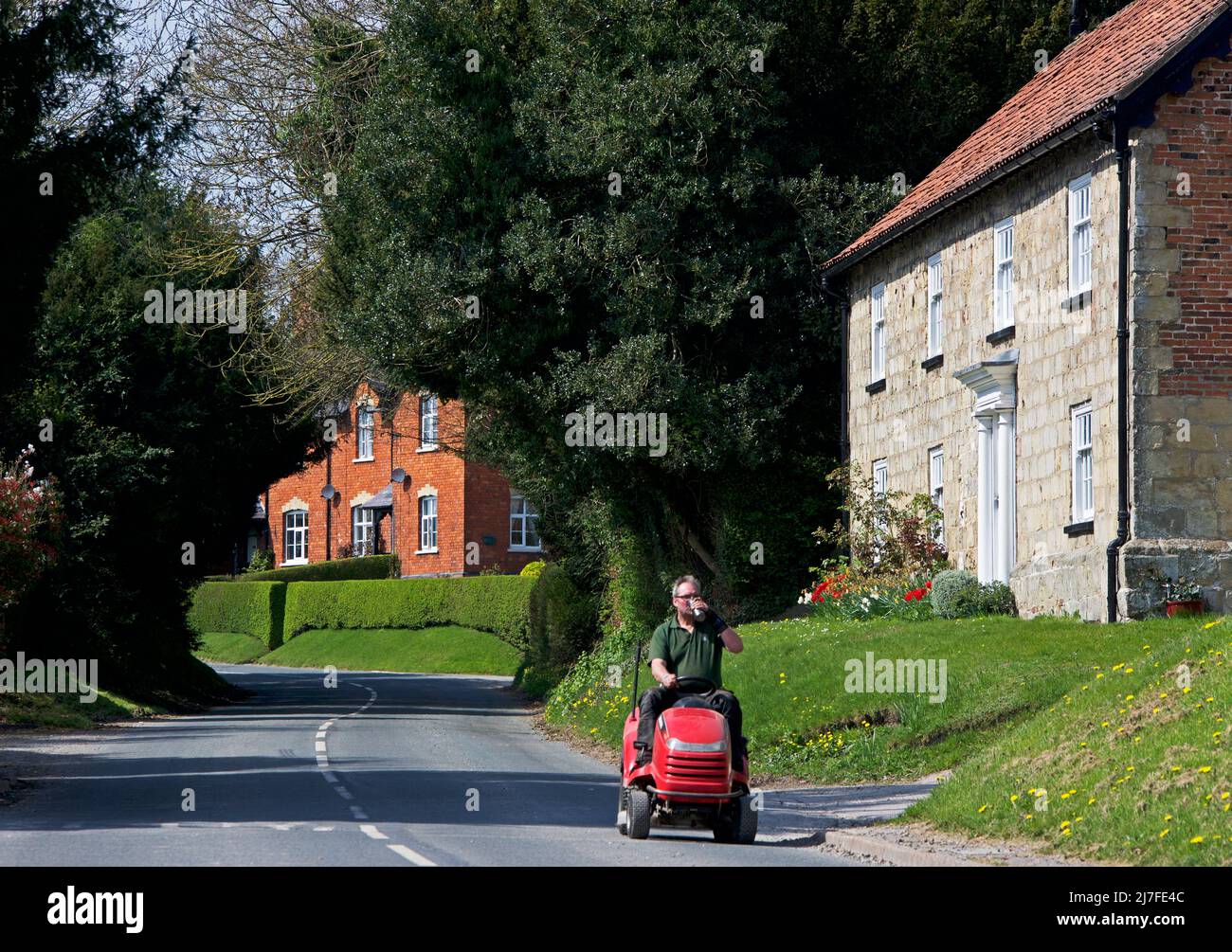 Homme et tondeuse autoportée dans le village de Warter, East Yorkshire, Angleterre Banque D'Images