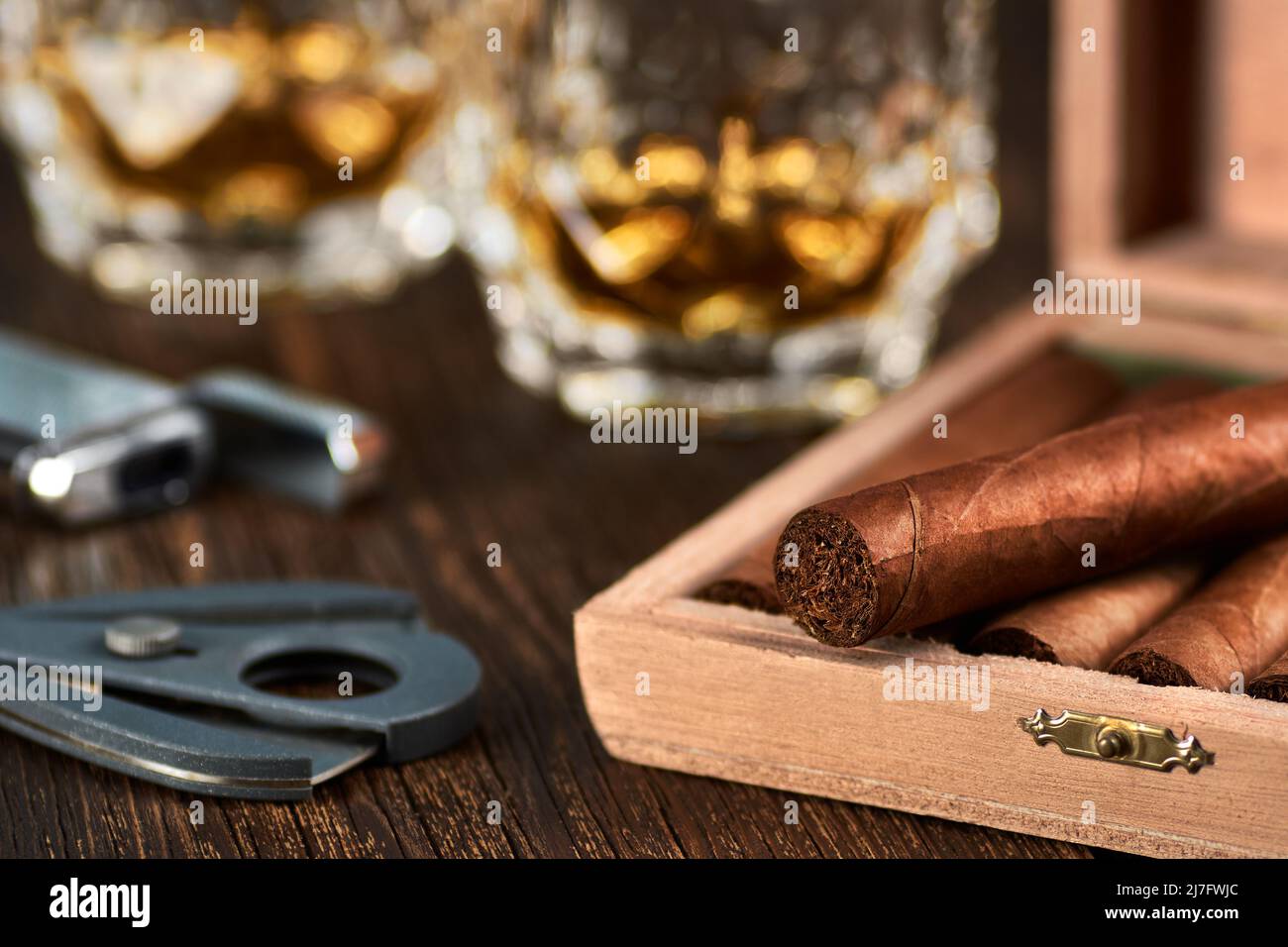 Vue sur une boîte en bois avec des cigares cubains, un briquet et un couteau. Encore plus de vie avec deux verres de whisky sur la table. Banque D'Images