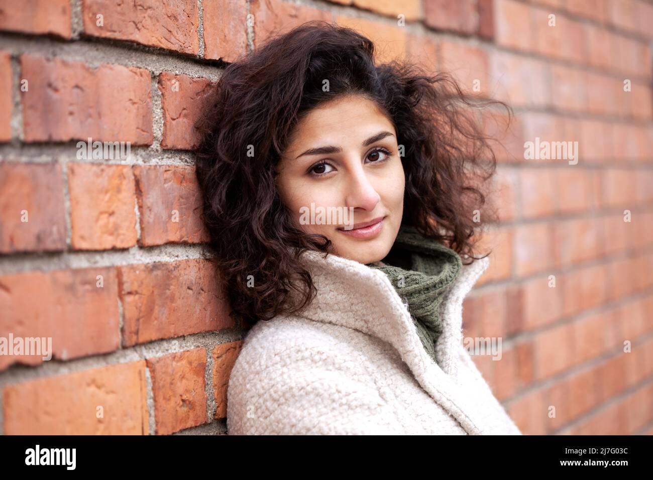 Portrait of young woman leaning against brick wall Banque D'Images