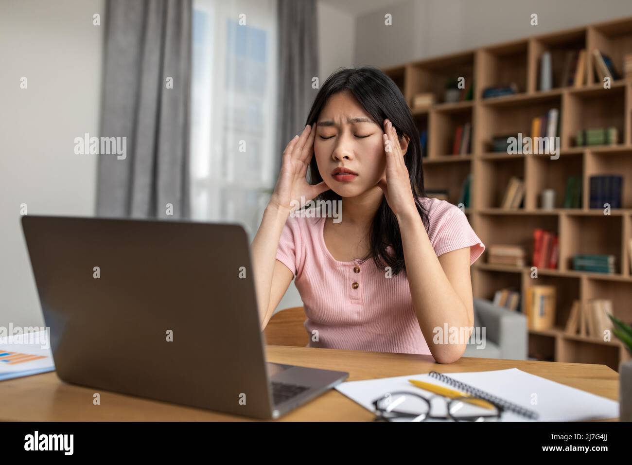 Contrainte d'échéance. Une jeune femme coréenne se sentait fatiguée après avoir travaillé sur un ordinateur portable, avoir des maux de tête et toucher des temples Banque D'Images