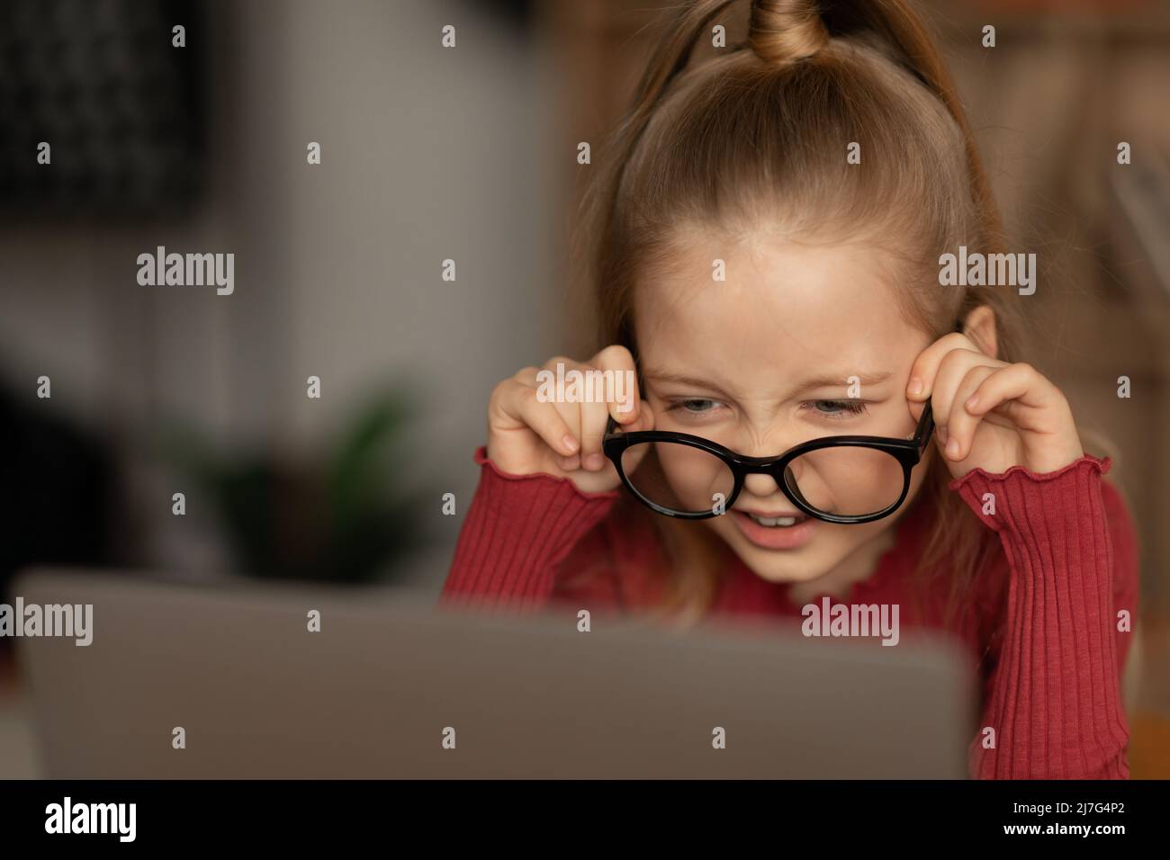 Petite fille avec une mauvaise vue portant des lunettes de vue en utilisant un ordinateur portable à l'intérieur Banque D'Images