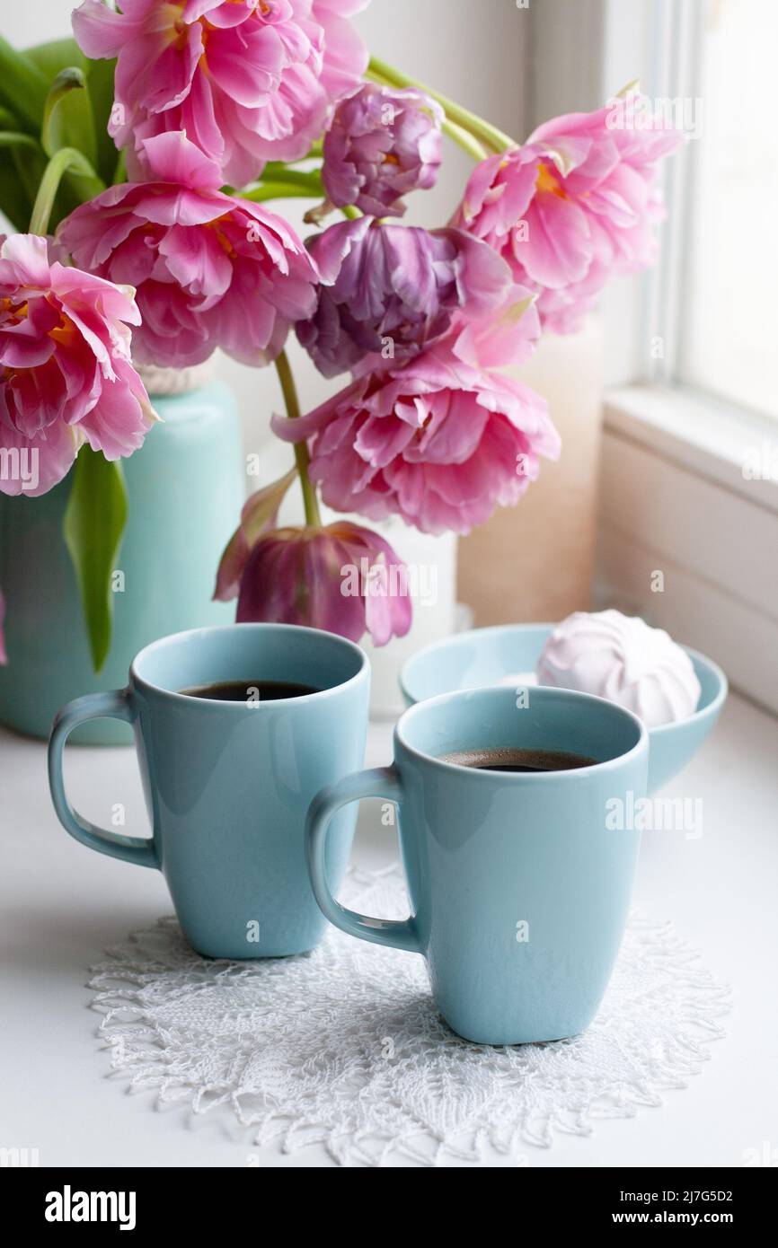 Deux tasses de café noir et un délicat guimauve pour le petit déjeuner sont à côté d'un beau bouquet de tulipes roses dans un vase bleu. Banque D'Images