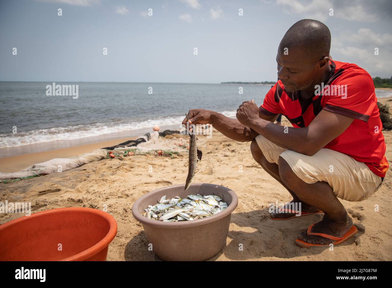 Le pêcheur africain regarde le poisson qu'il vient de prendre dans un seau, le pêcheur à la plage pendant qu'il travaille Banque D'Images