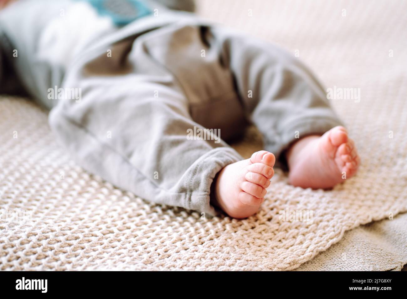 Photo courte du nouveau-né pieds nus portant un body gris couché sur un tissu tricoté en coton beige. Gros plan des petits pieds de bébé sur le lit. Heure du coucher, m Banque D'Images