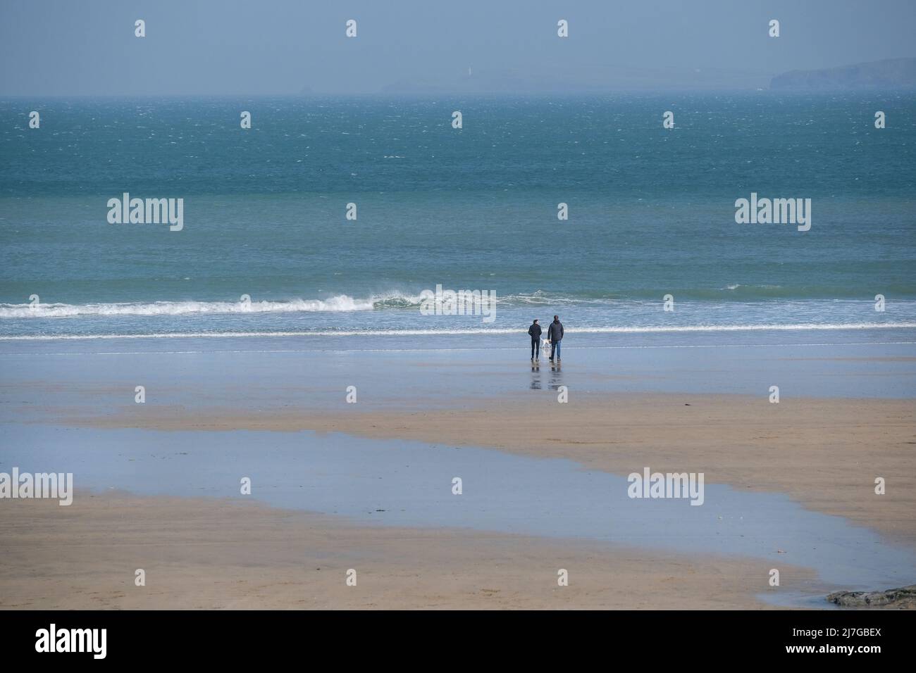 Vu de loin deux hommes et un chien debout sur le rivage à marée basse sur la plage de Towan à Newquay, en Cornouailles, au Royaume-Uni. Banque D'Images