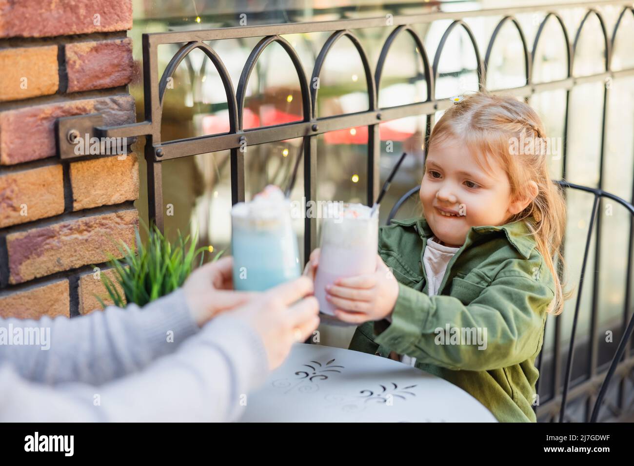 une jeune fille gaie qui toasque avec des verres de milkshake avec une maman floue dans un café de rue Banque D'Images