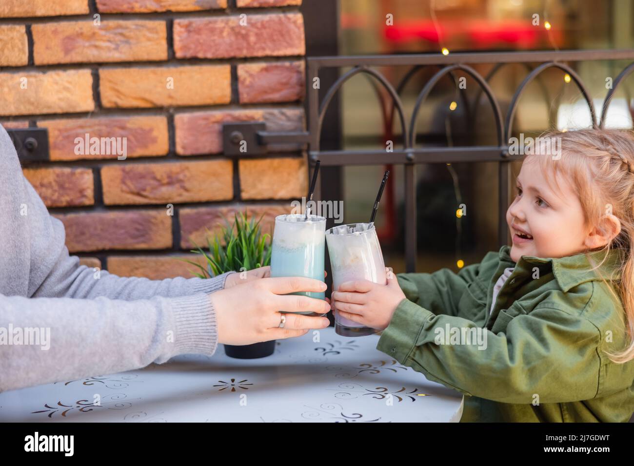 bonne fille en toaster avec des verres de milkshake tout en étant assise avec la mère dans le café de rue Banque D'Images
