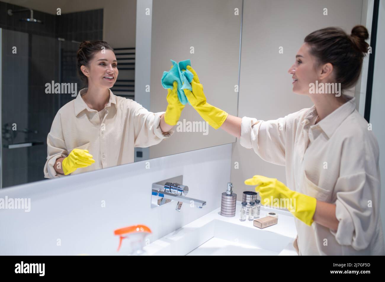 Une jeune femme mignonne à nettoyer le miroir dans la salle de bains Banque D'Images