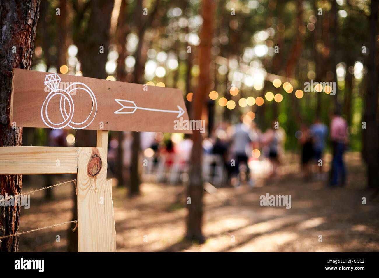 Panneau en bois avec anneaux de mariage sur le lieu de la cérémonie. Bannière de fête de mariage post . Bannière d'informations de direction pour les clients dans la forêt de pins en plein air. Rustique Banque D'Images