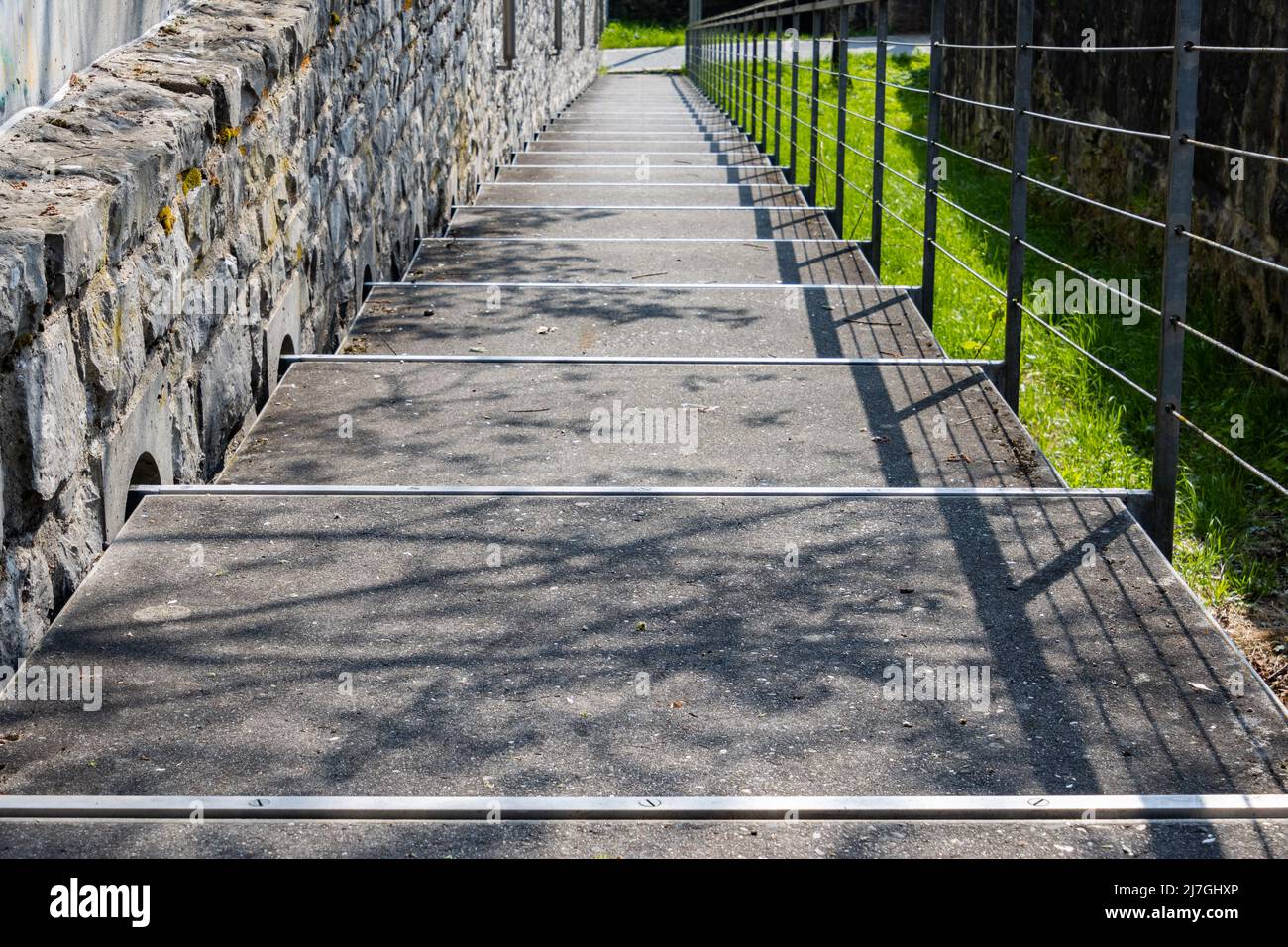 Passerelle piétonne menant vers le bas entre un mur en pierre naturelle et une main courante en acier Banque D'Images
