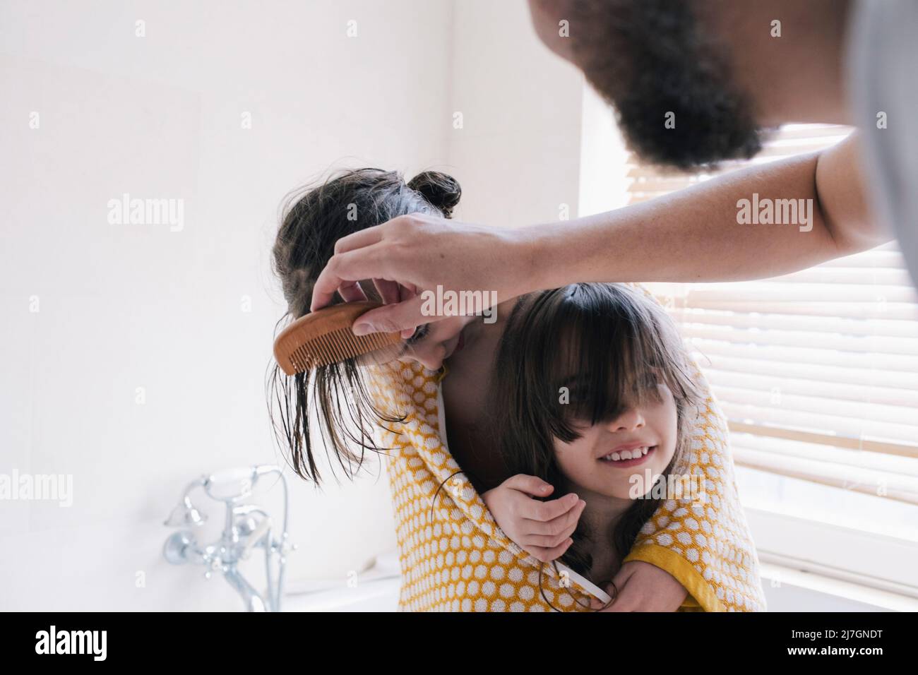 Homme peignant les cheveux de la fille dans une serviette avec une sœur dans la salle de bains Banque D'Images