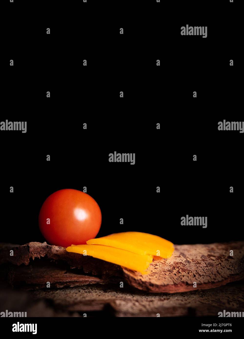 Fromage et tomate placés sur un morceau d'écorce sur fond noir Banque D'Images