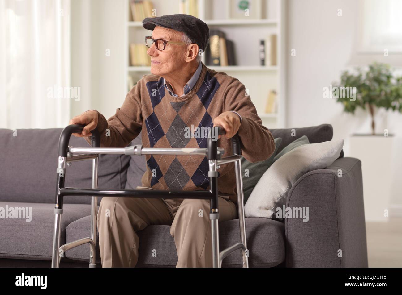 Homme âgé assis sur un canapé et tenant sur un marcheur Banque D'Images