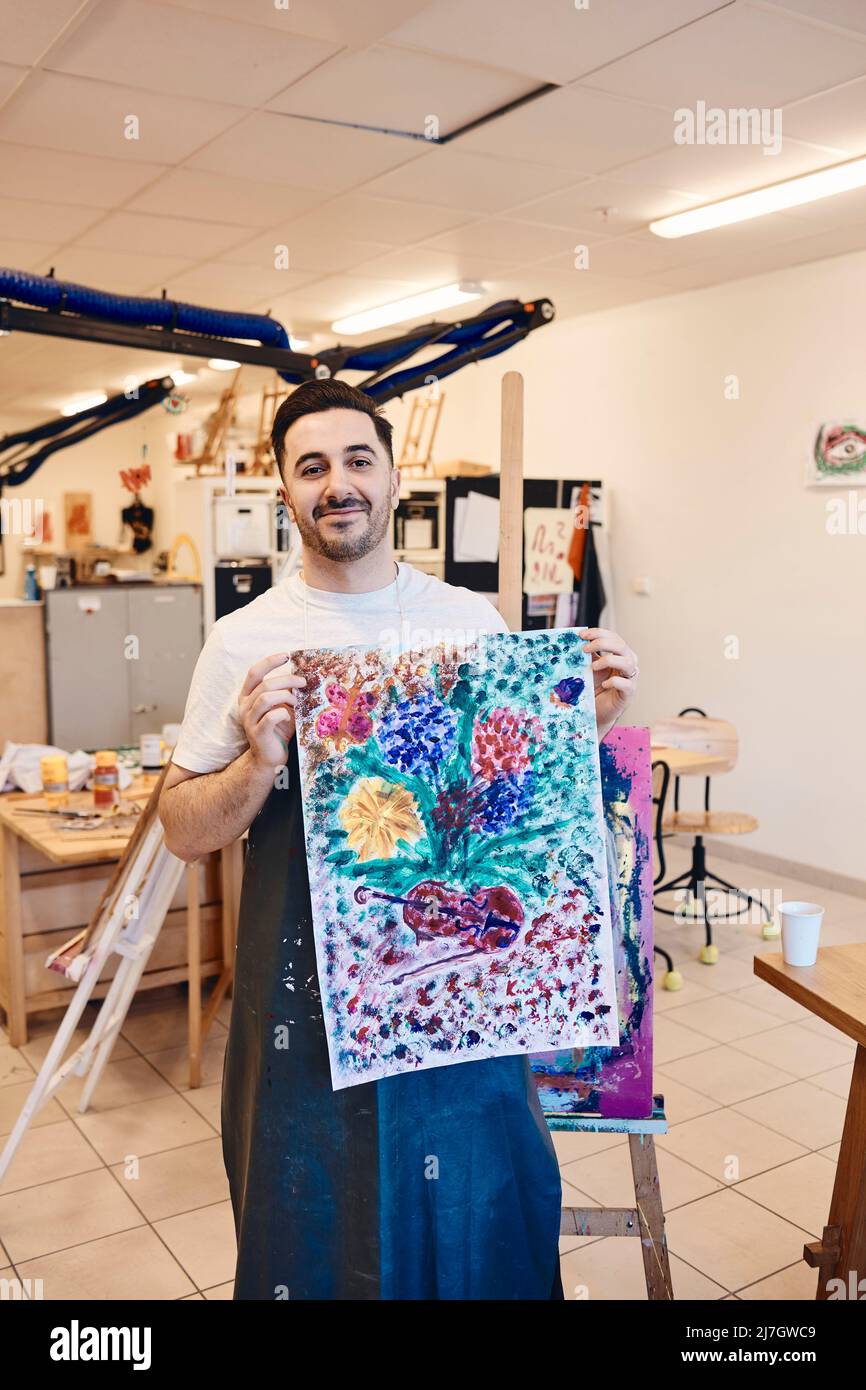 Portrait d'un peintre masculin souriant montrant une peinture de toile multicolore en classe d'art Banque D'Images