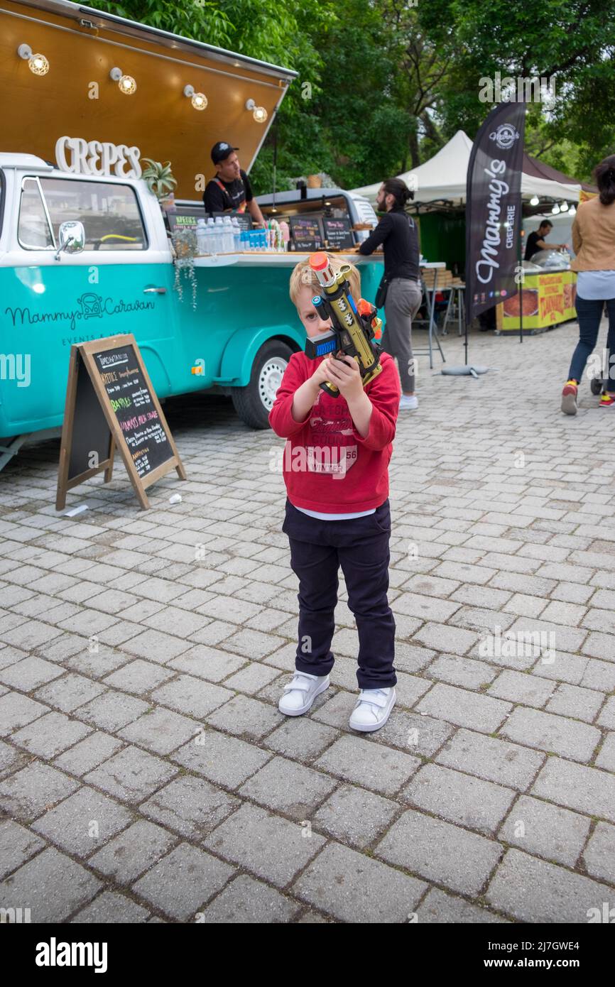 Mignon petit garçon jouant avec son fusil de jouet devant une camionnette vokswagen T2 lors d'un festival Banque D'Images