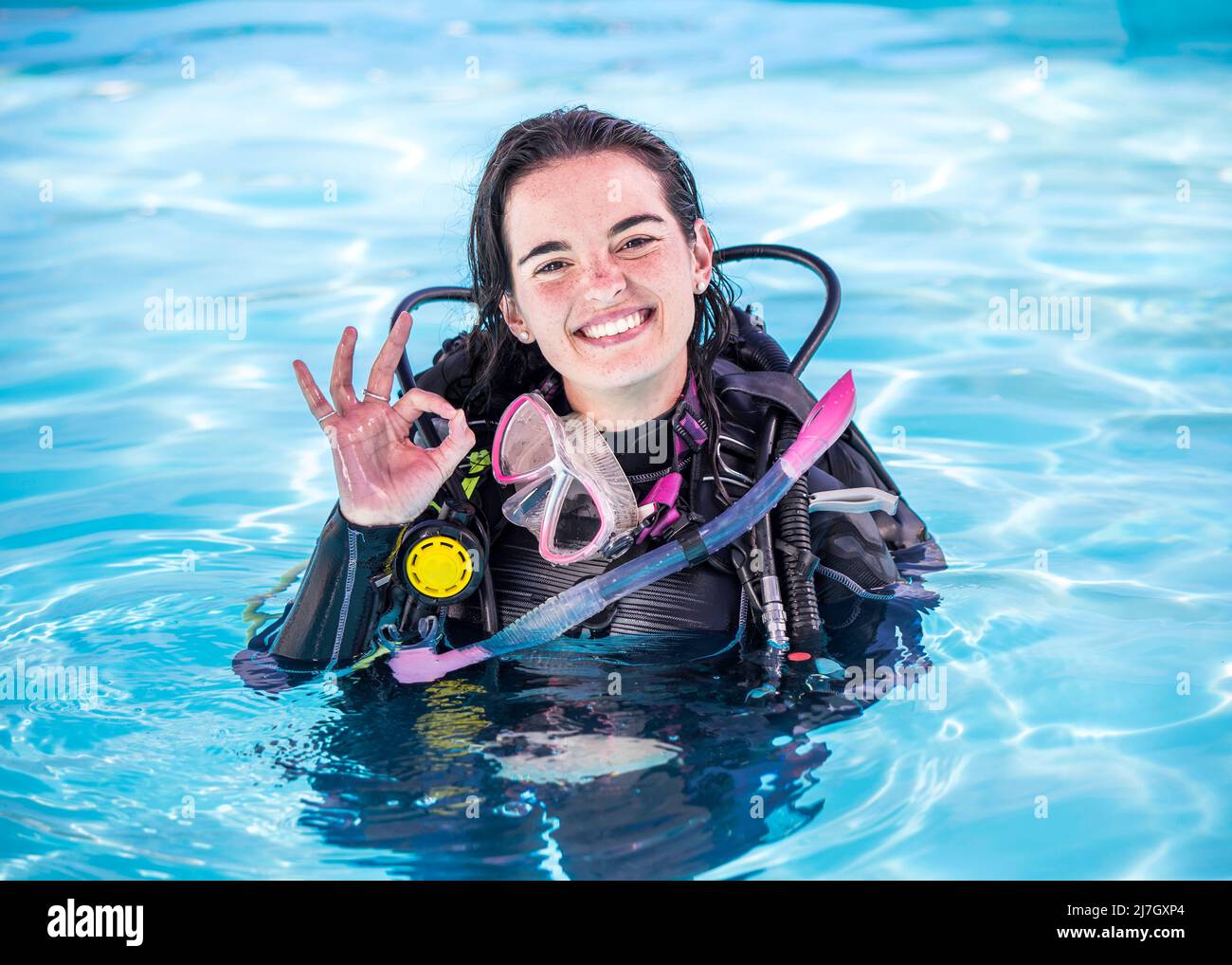 Jeune femme avec du matériel de plongée dans une piscine souriant à la caméra montrant le panneau OK Banque D'Images
