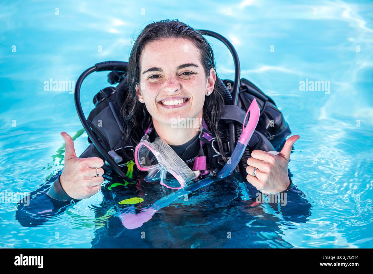 Jeune femme avec du matériel de plongée dans une piscine souriant à l'appareil photo montrant les pouces vers le haut Banque D'Images