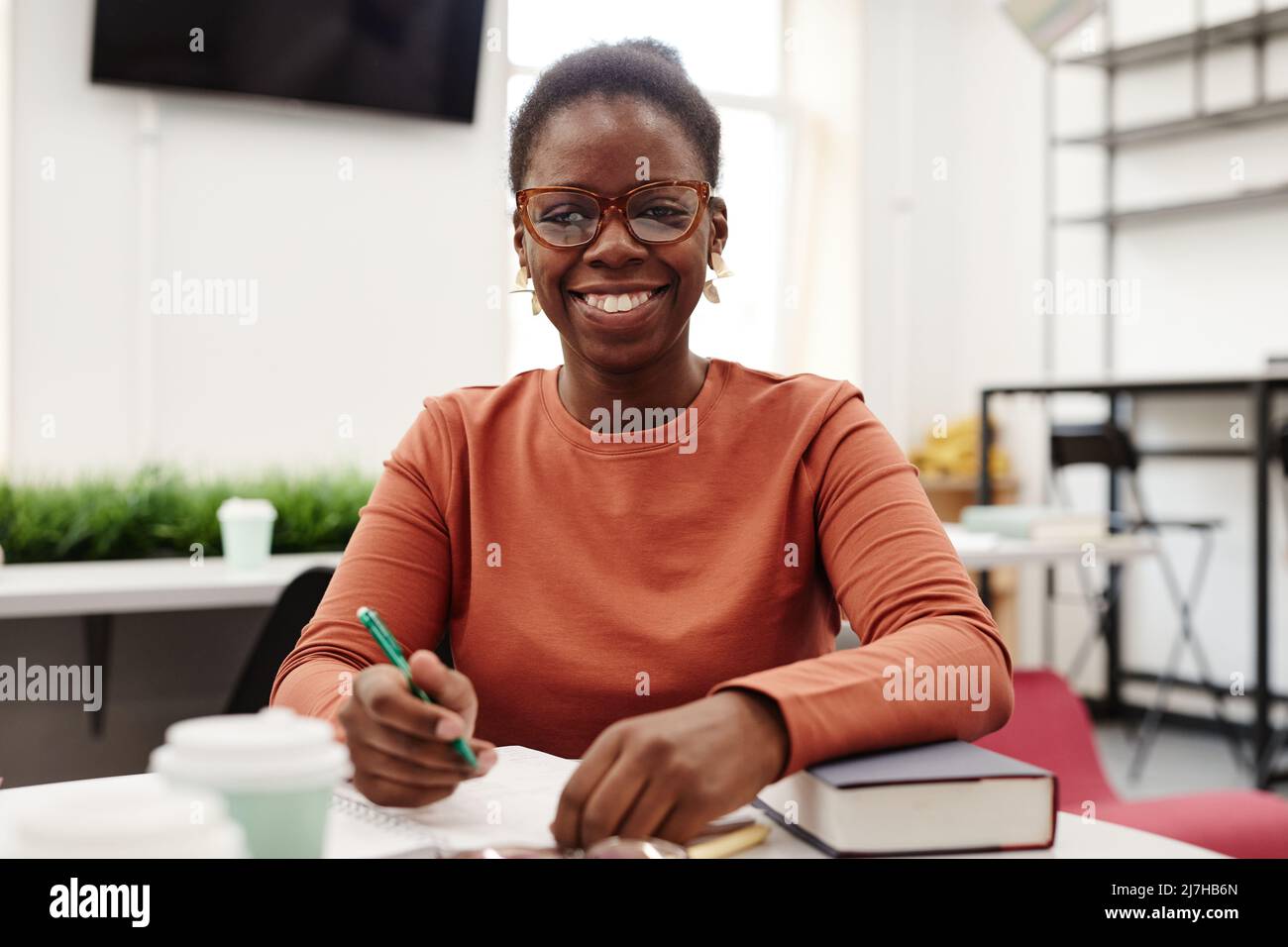 Portrait de la jeune femme noire étudiant à l'université et souriant avec joie à l'appareil photo Banque D'Images