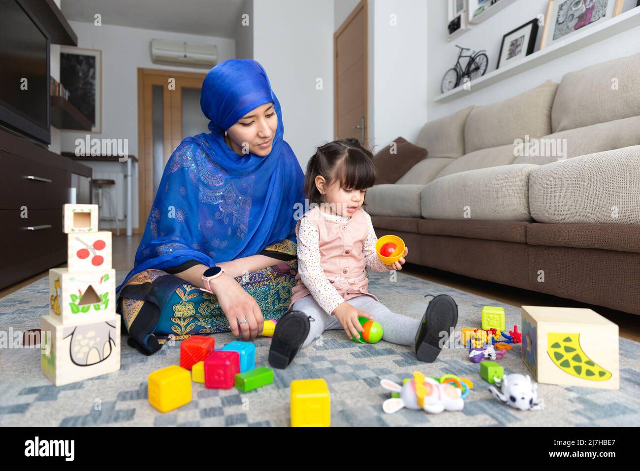 Jeune musulmane jouant avec sa jeune fille dans le salon. Famille monoparentale à la maison. Banque D'Images