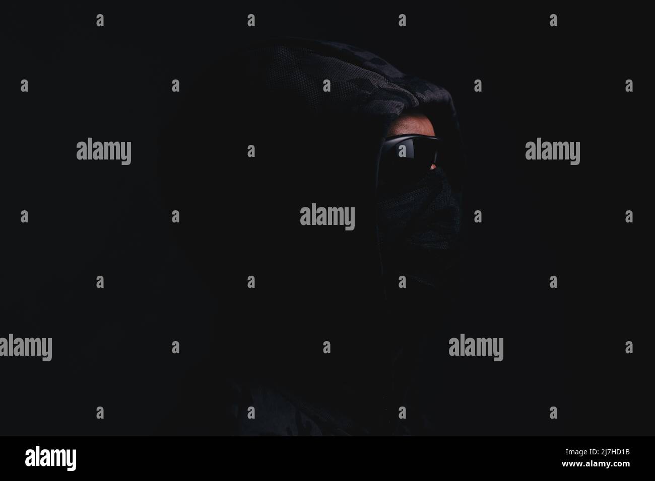 Homme élégant en pull à capuche foncé avec des lunettes noires et masque arrière-plan sombre, hacker, attaquant et bandit Banque D'Images