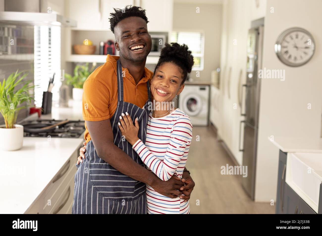 Portrait d'un jeune homme afro-américain joyeux portant un tablier embrassant une jeune amie dans la cuisine Banque D'Images