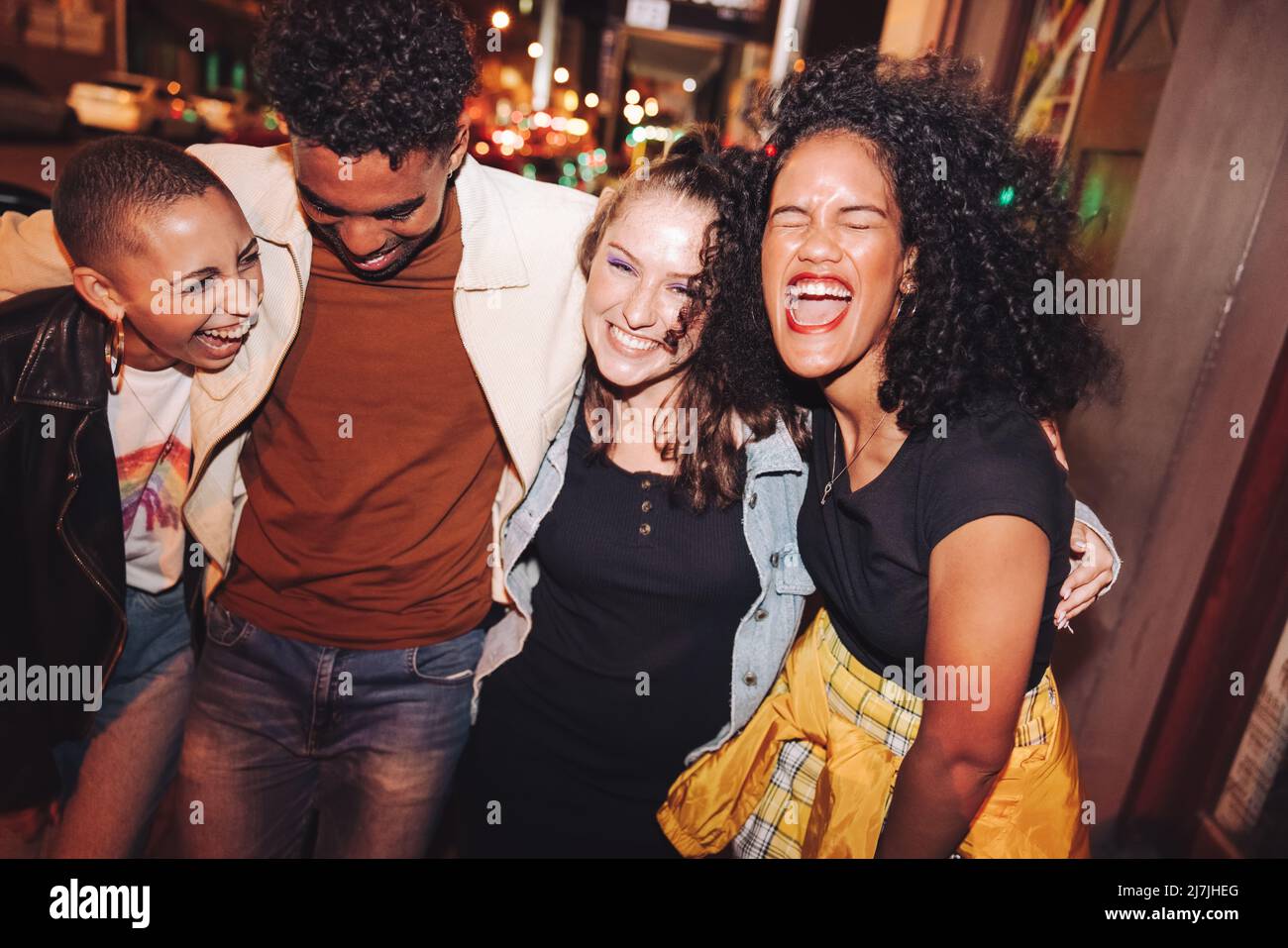 Le vendredi soir, c'est amusant. Groupe de jeunes dynamiques riant joyeusement en marchant ensemble dans la ville la nuit. Quatre amis multiculturels qui vont Banque D'Images