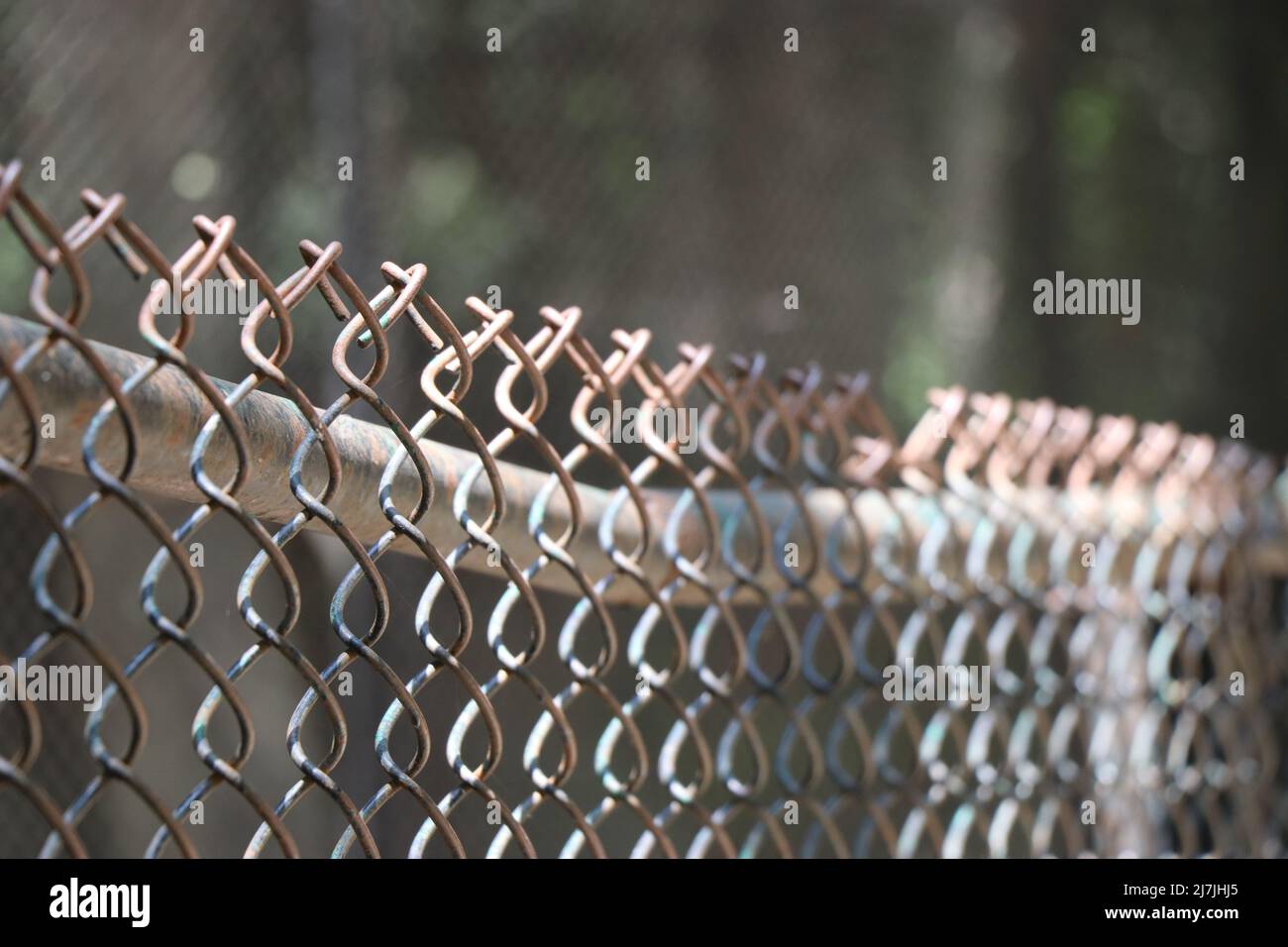 Vue rapprochée d'une clôture protégeant une propriété. Clôture à maillons de chaîne avec fil barbelé et poutres de lumière du soleil Banque D'Images