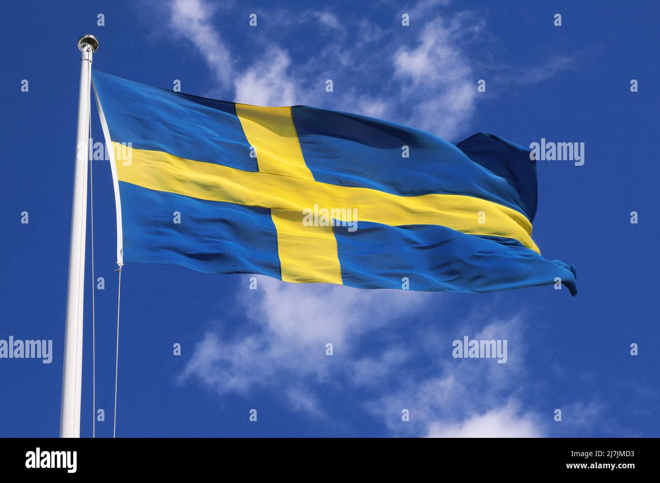 Vue rapprochée en petit angle d'un drapeau national suédois hissé volant dans le vent contre un ciel bleu avec des nuages clairs. Banque D'Images