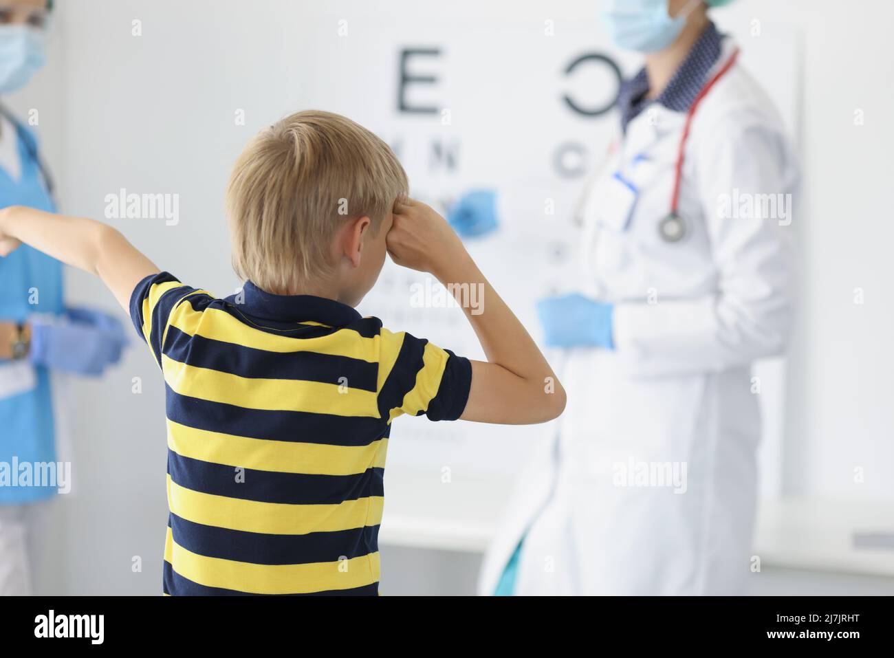 Garçon sur rendez-vous à la clinique, cabinet d'oculiste, oeil de fermeture de diagnostic de vue et dire à haute voix lettre à bord Banque D'Images