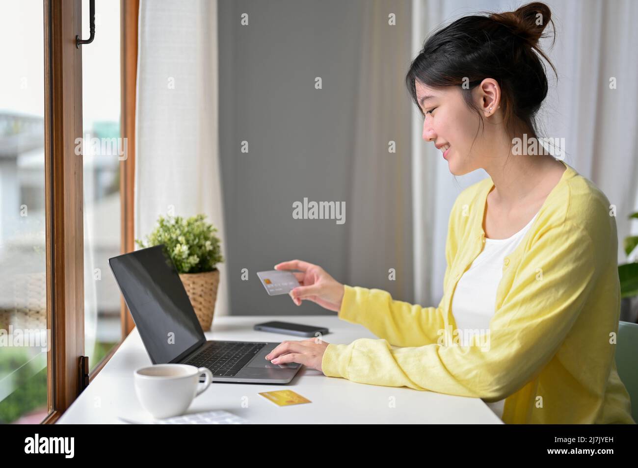 Vue arrière, belle femme asiatique millénaire assise dans le café, profiter de shopping sur le site Web en ligne et payer en ligne avec sa carte de crédit. Banque D'Images