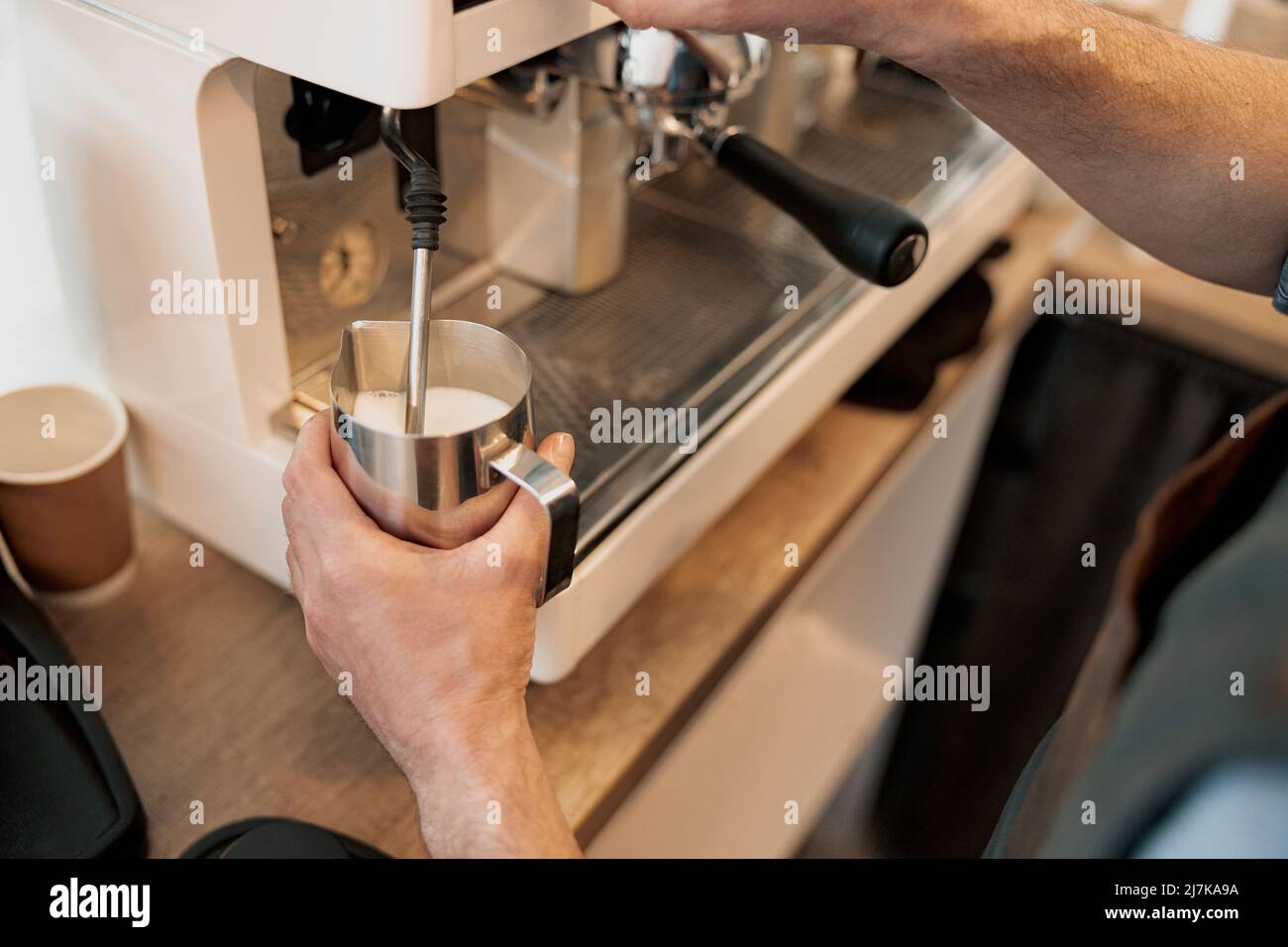 Gros plan des mains du barista chauffant le lait dans le pichet à la vapeur Banque D'Images