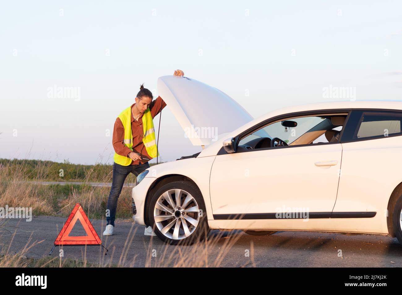 Homme à la recherche d'une voiture cassée sur le côté de la route dans un paysage vide avec capot de voiture ouvert essayant de réparer après avoir appelé l'assistance Banque D'Images
