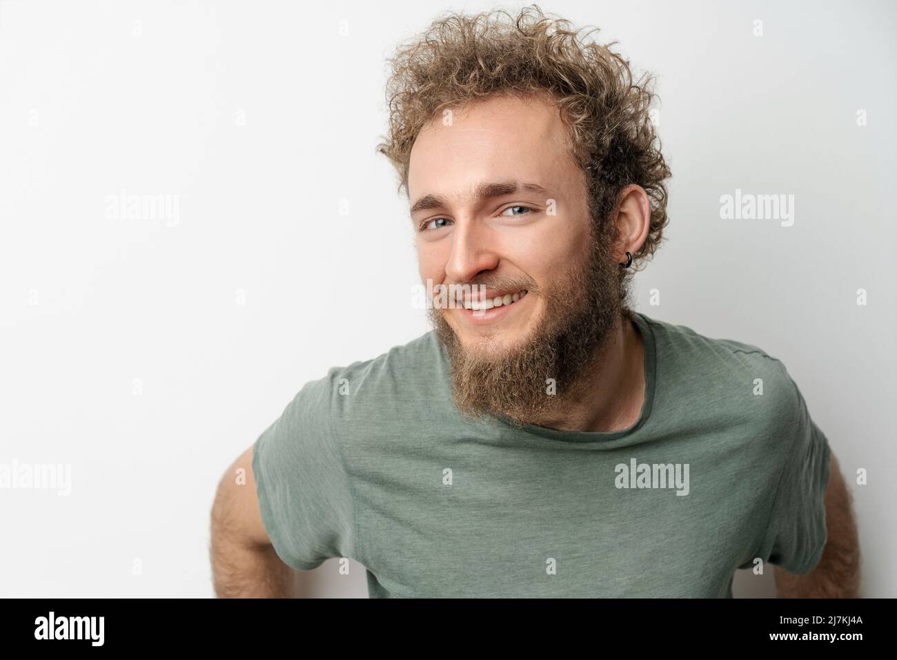 Jeune beau avec des yeux bleu vif barbu sauvage cheveux bouclés homme isolé sur fond blanc. Jeune homme pensant dans un t-shirt vert sur fond blanc. Copier l'espace. Banque D'Images