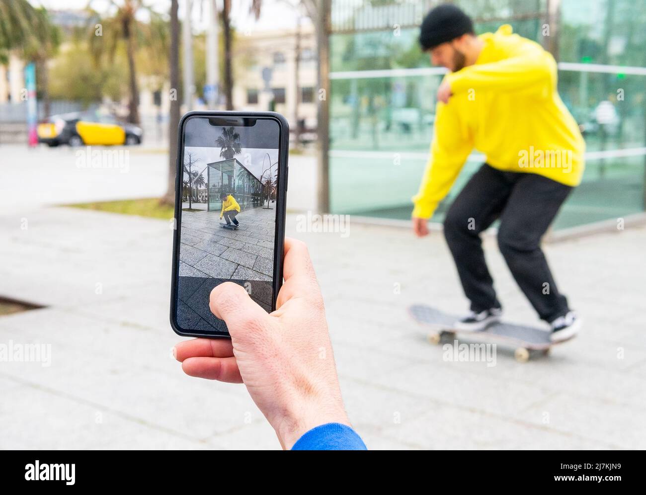 Personne anonyme prenant des photos avec le téléphone d'un patineur sur un chandail jaune skate dans la rue Banque D'Images