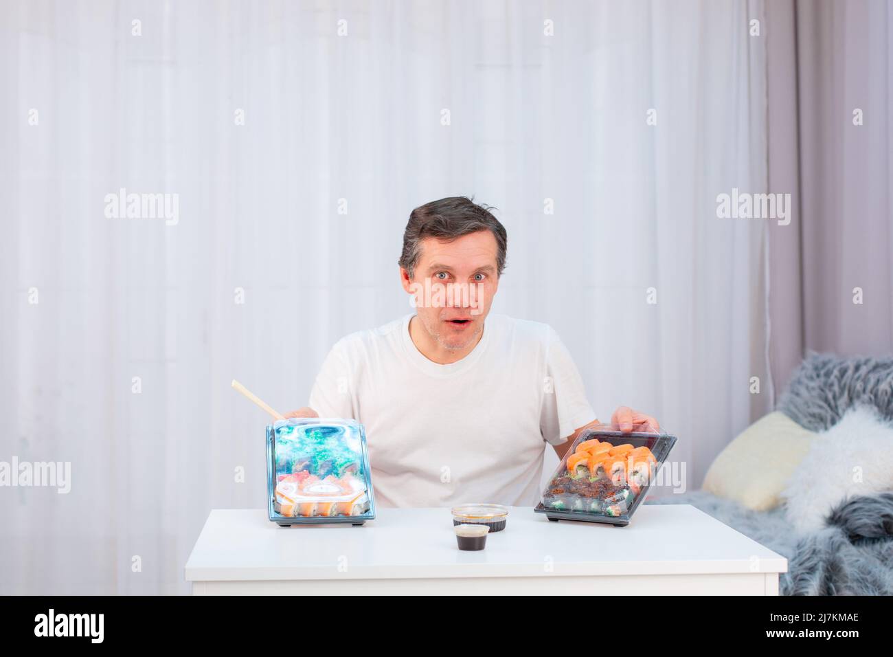 Un homme caucasien âgé writhes visages drôles, regardant les sushis d'une livraison Banque D'Images