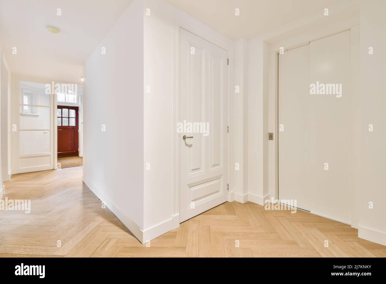 Couloir d'appartement élégant et lumineux avec murs blancs et porte vitrée d'entrée près des chambres avec miroir et chaise à la maison Banque D'Images