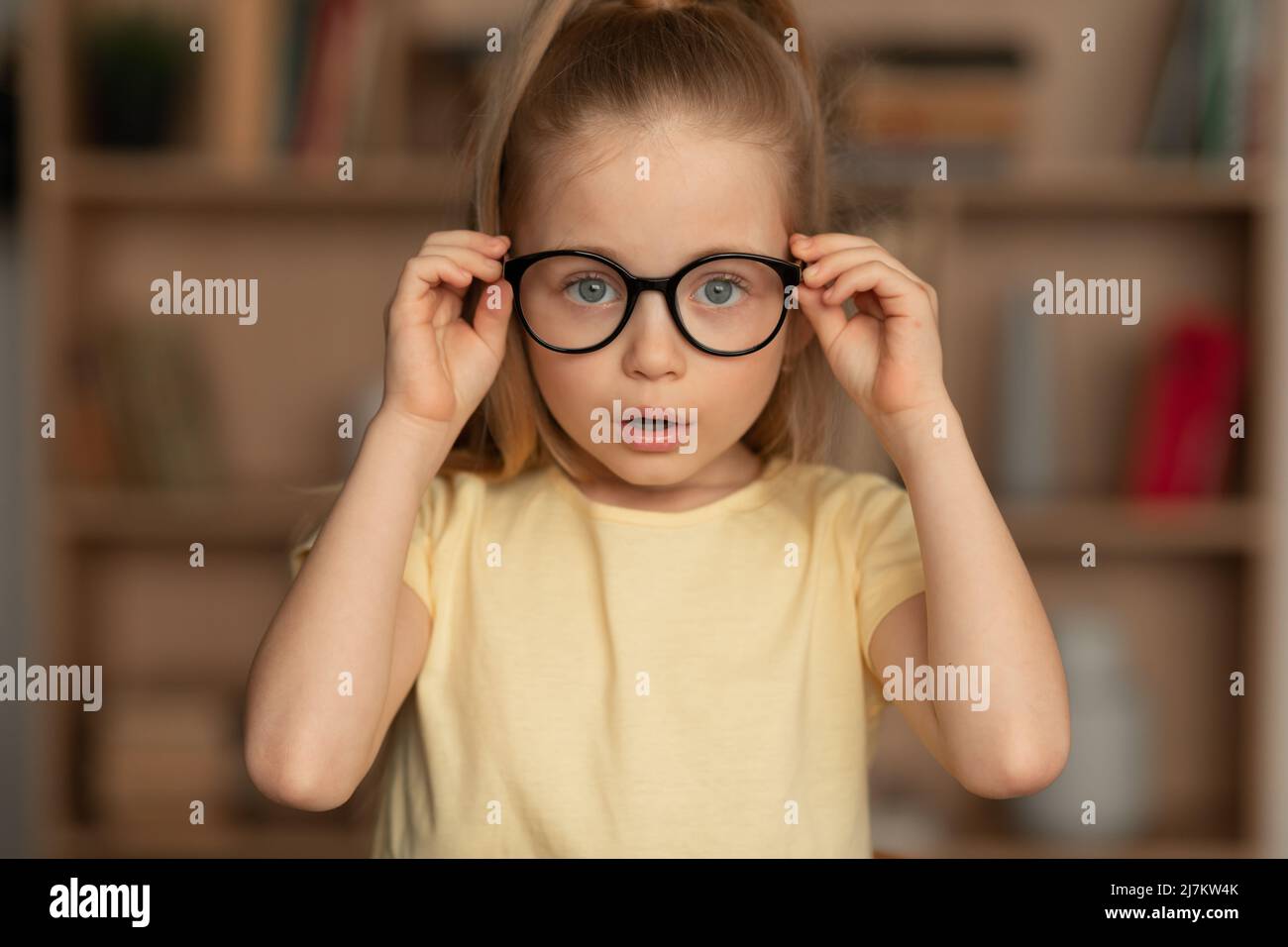 Petite fille portant des lunettes ayant une mauvaise vue posant à la maison Banque D'Images