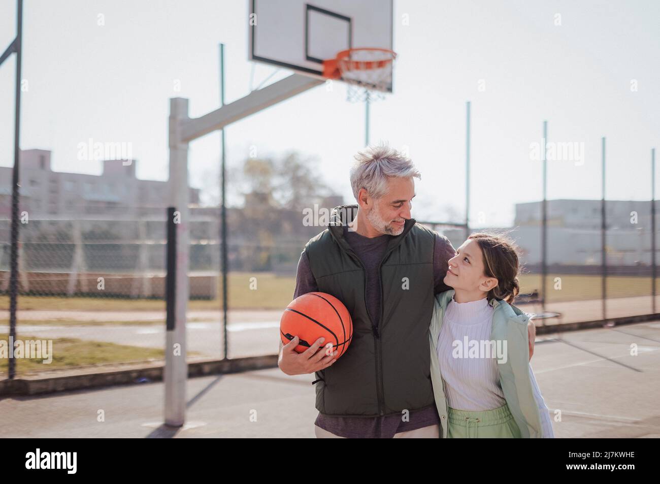 Un père heureux et une fille adolescente embrassant et regardant l'appareil photo à l'extérieur du terrain de basket-ball. Banque D'Images