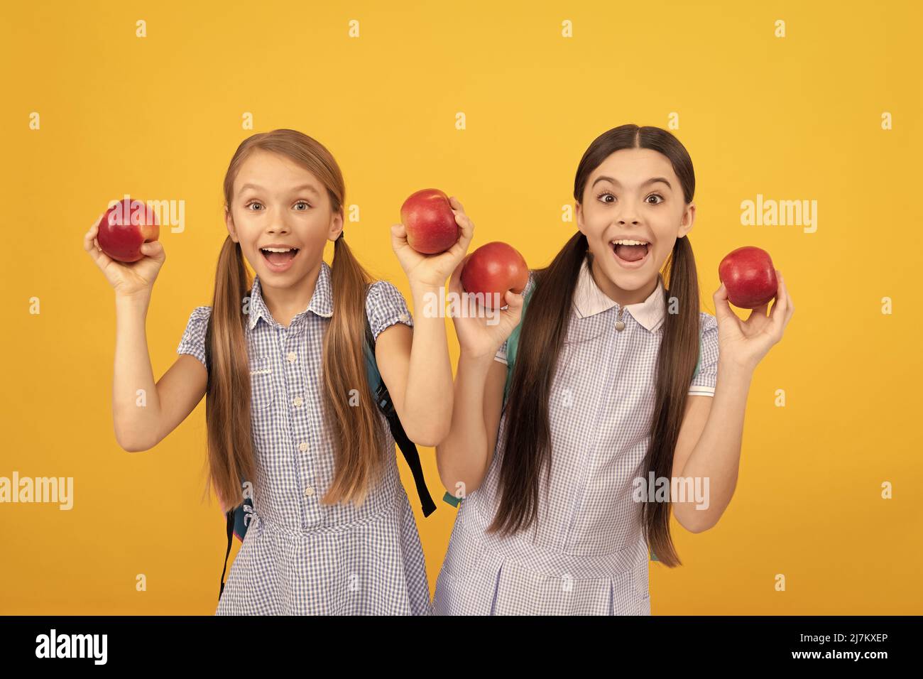 Les enfants heureux tiennent des pommes pour une collation saine de retour à l'école fond jaune, l'alimentation scolaire Banque D'Images