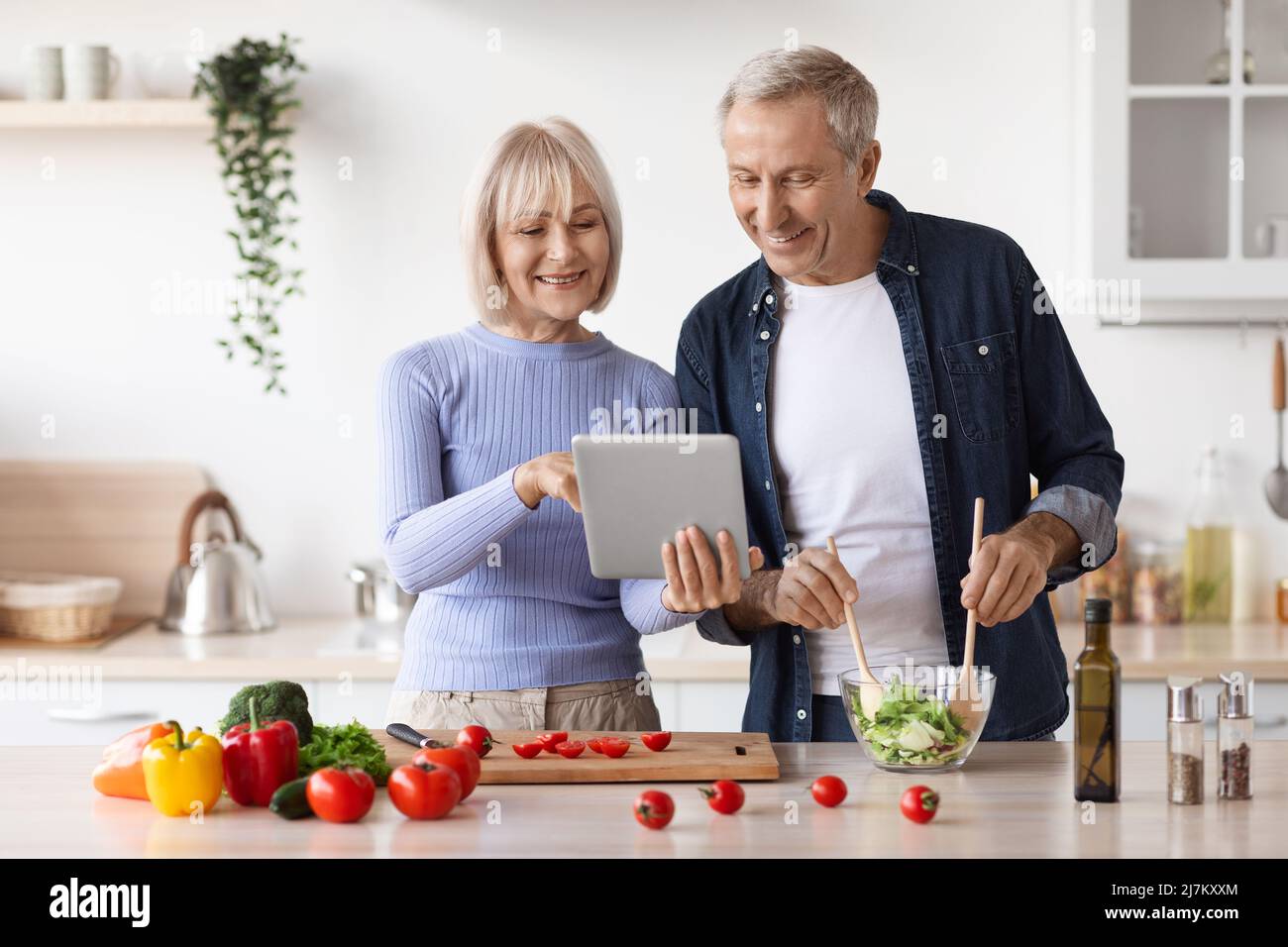 Un couple senior lisant un blog alimentaire sur une tablette numérique dans la cuisine Banque D'Images