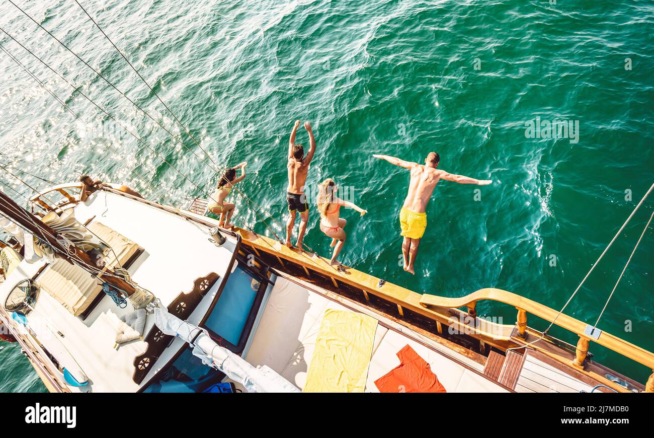Vue imprenable sur les amis aventureux branchés qui sautent du voilier en bord de mer - les garçons et les filles du millénaire s'amusent à une soirée en bateau exclusive Banque D'Images