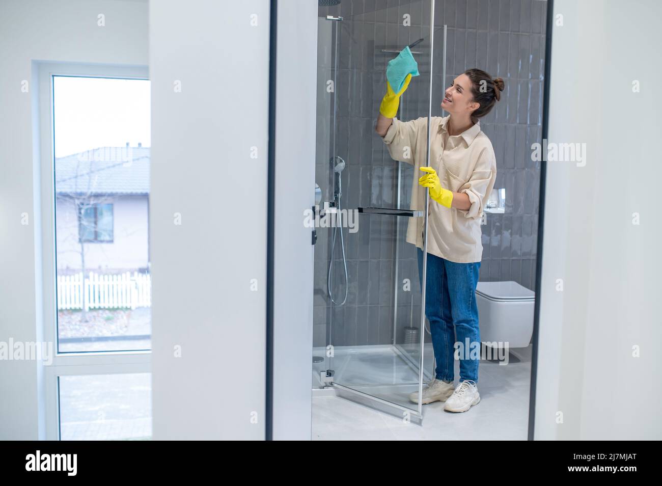 Une jeune femme nettoie la cabine de douche à la maison et a l'air occupée Banque D'Images