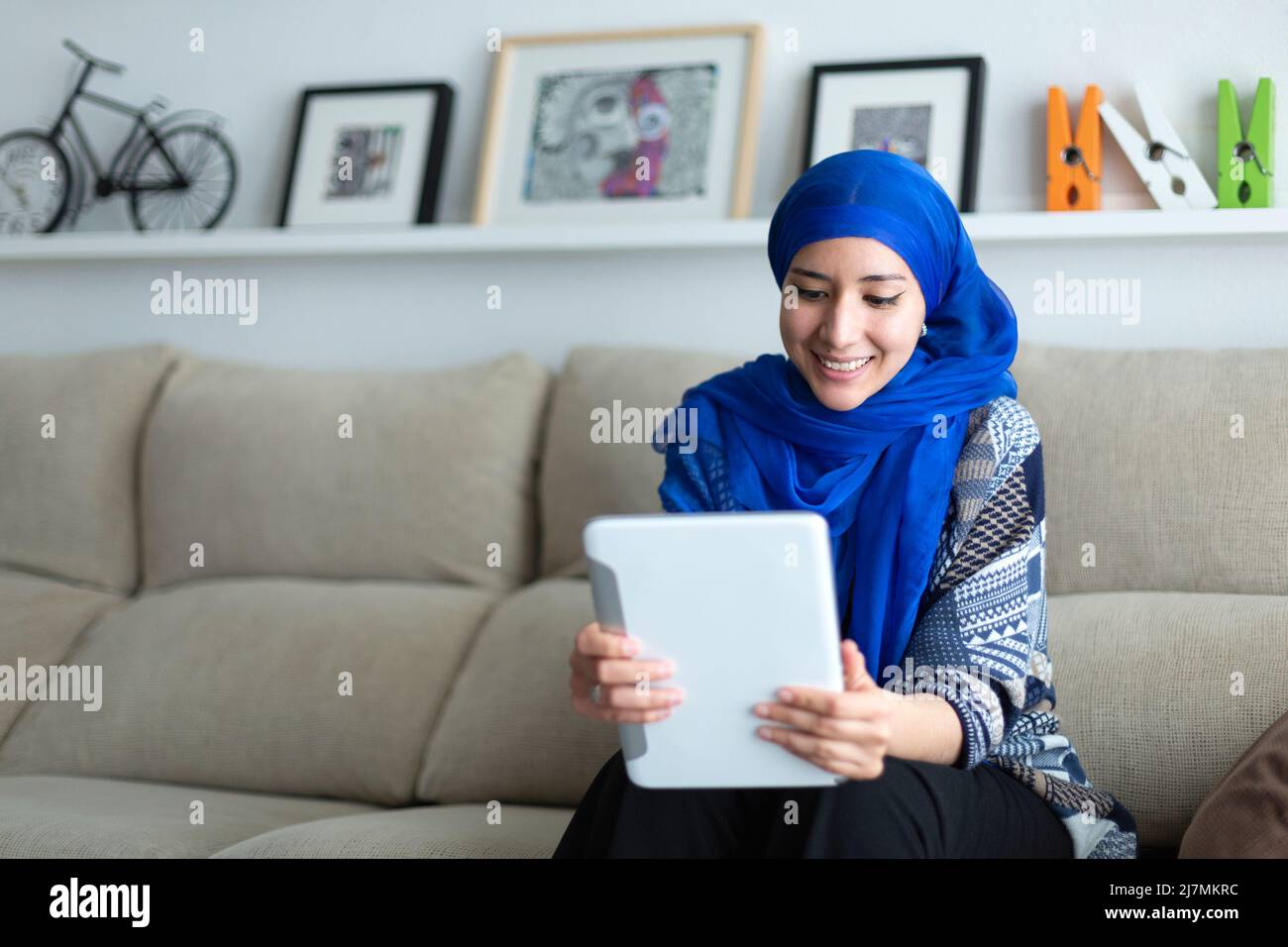 Jeune femme musulmane souriante utilisant une tablette numérique à la maison. Technologie et style de vie. Espace pour le texte. Banque D'Images