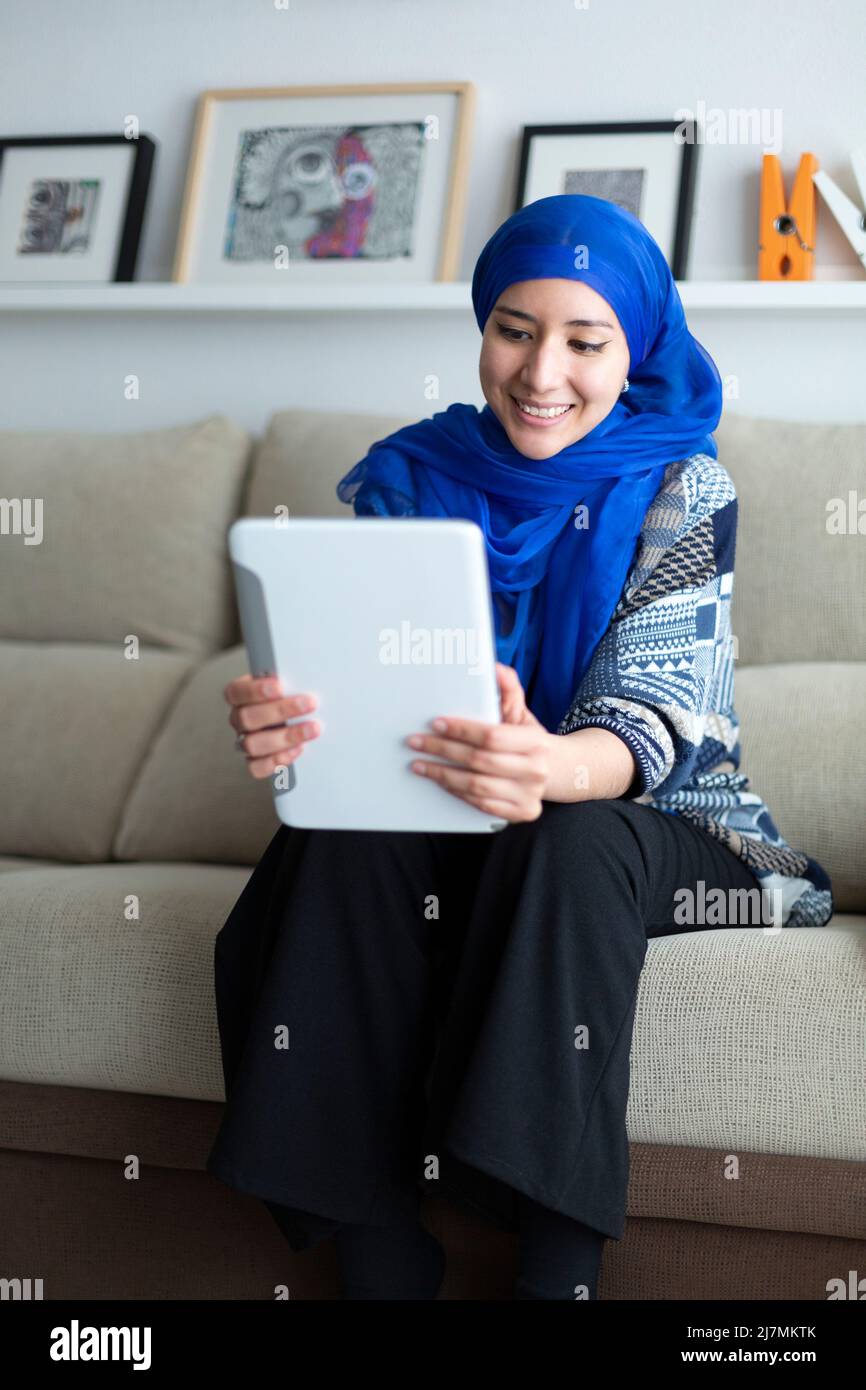 Jeune femme musulmane souriante utilisant une tablette numérique à la maison. Technologie et style de vie. Banque D'Images