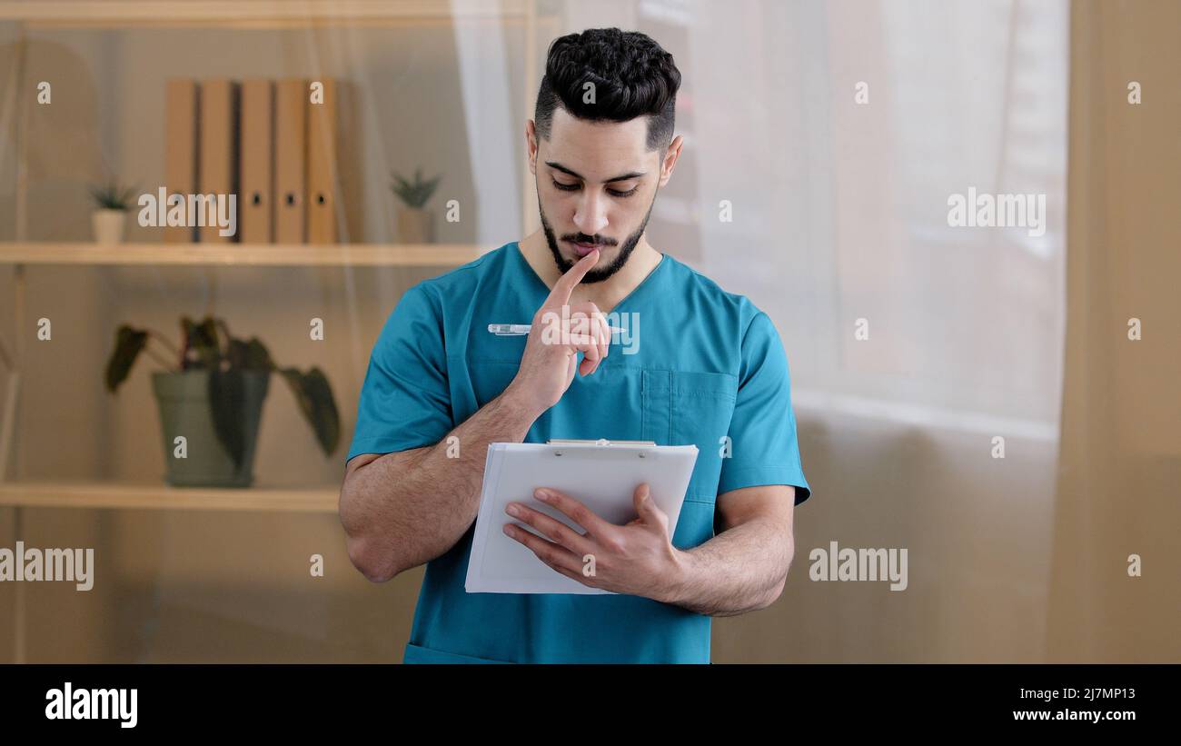 Hispanique médecin homme médecin homme thérapeute médical porter uniforme debout dans la clinique de l'hôpital écrire des notes remplir le formulaire médical avis d'assurance détaillé Banque D'Images