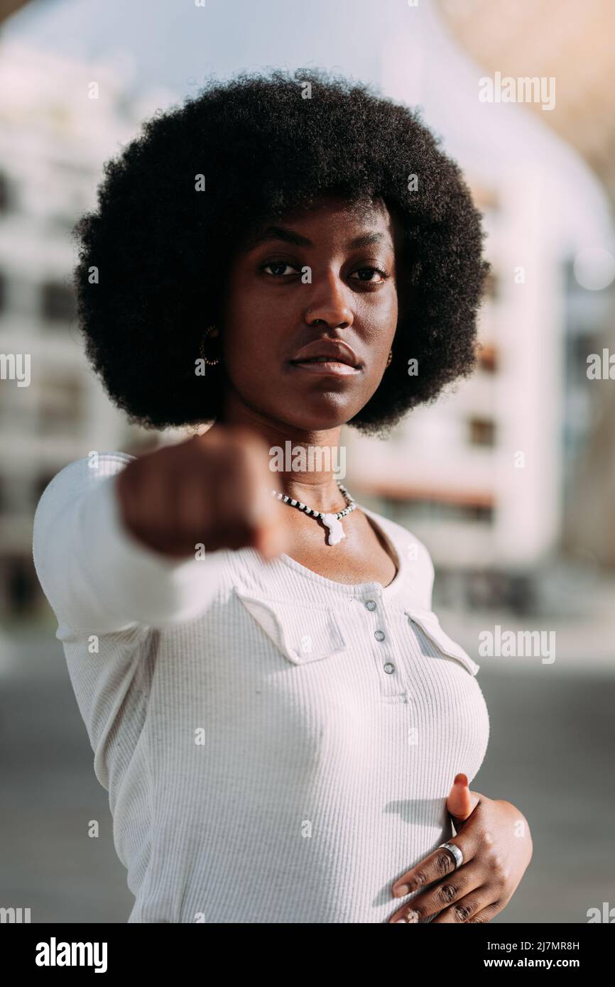 Portrait d'une jeune femme noire aux cheveux d'afro en gestant avec son poing fermé symbolisant la force. Concept de puissance de fille. Verticale Banque D'Images