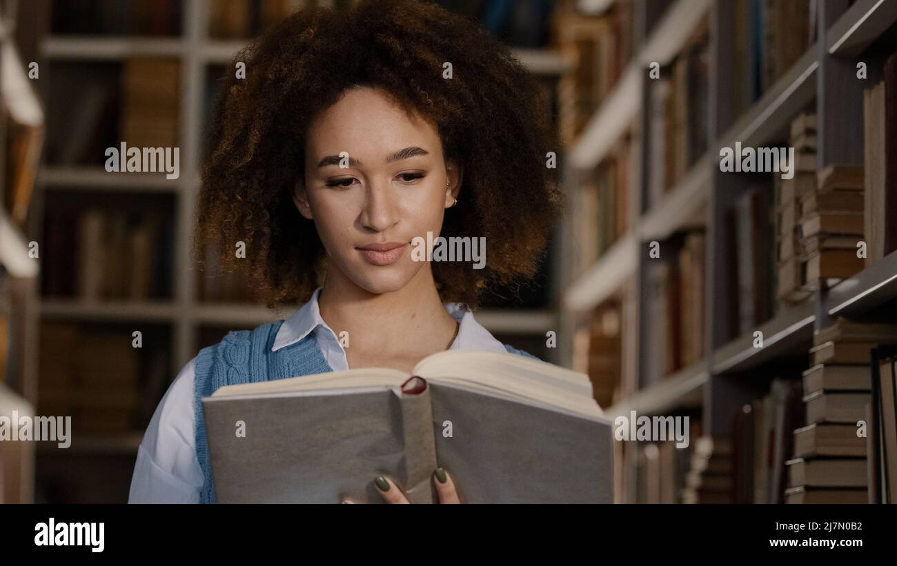 Une jeune fille afro-américaine élève dans une bibliothèque publique d'université intéressée par les lectures livre histoire intéressante regardant attentivement le manuel Banque D'Images